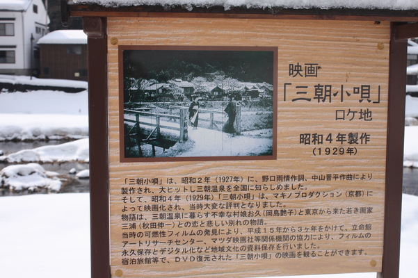 積雪の「三朝川」岸辺に立つ映画「三朝小唄」のロケ地説明版