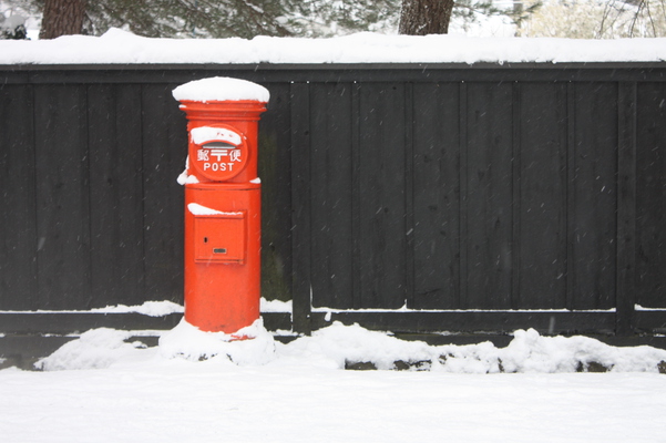 積雪の黒塀と赤いポスト