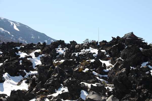 雪の溶岩原と浅間山観音堂（右奥）